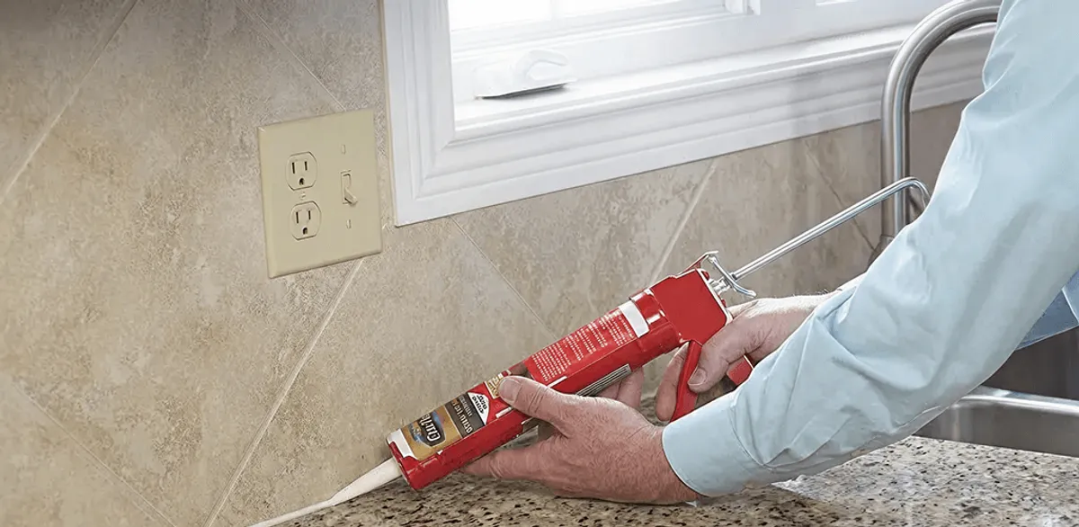 Handyman applying caulk along a kitchen backsplash and countertop seam in Saint Louis, MO